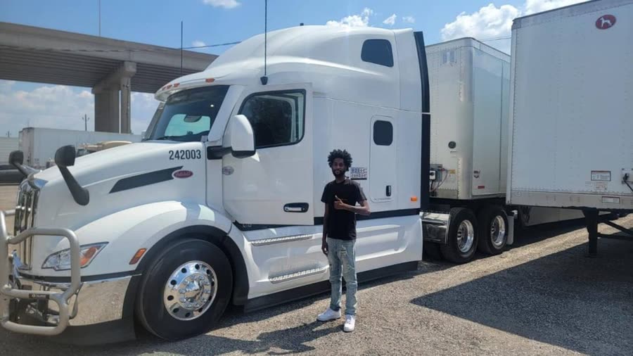 Driver giving a thumbs up next to a Peterbilt with a dry van trailer